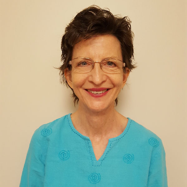 A woman with short hair and glasses wearing a blue shirt.